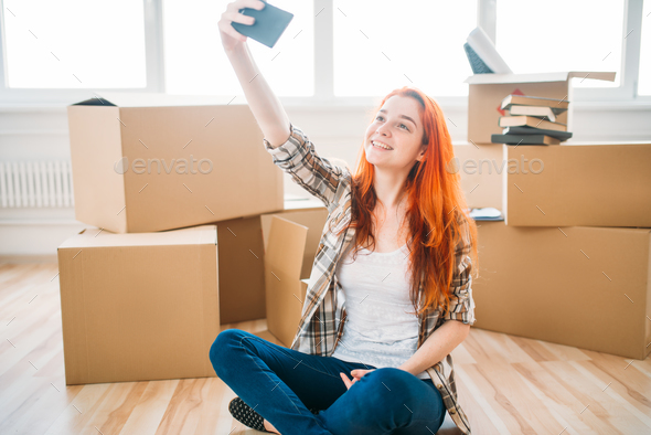 Woman among cardboard boxes makes selfie on camera - Stock Photo - Images