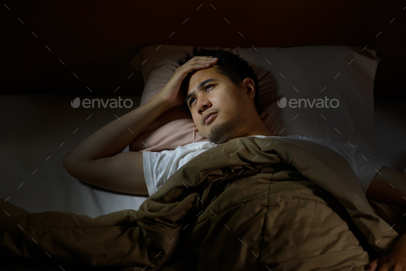 Depressed man suffering from insomnia lying in bed