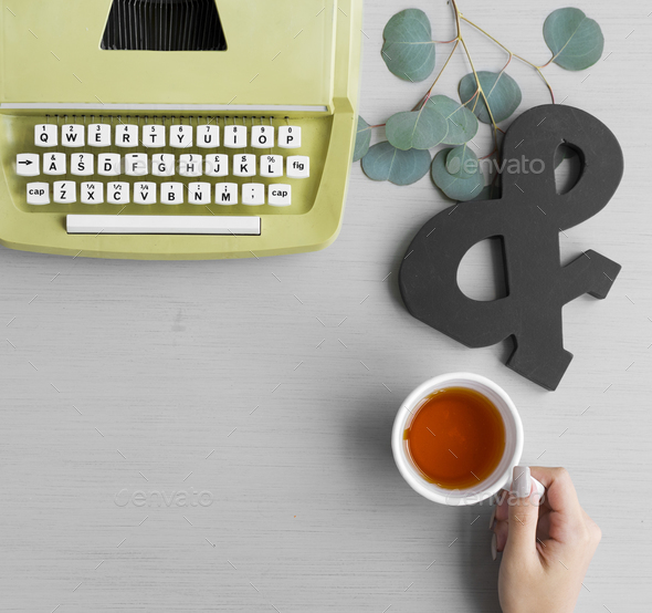 Retro Typewriter with Hand Holding Tea Cup on Gray Background