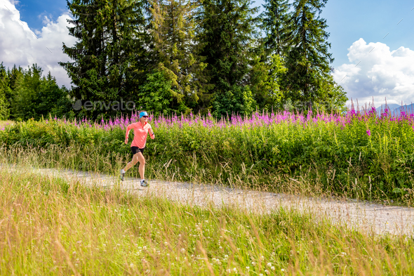 Young woman running on country road in mountains, summer day - Stock Photo - Images