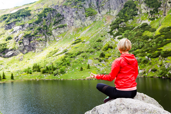 Woman meditating in yoga pose in front of mountain lake