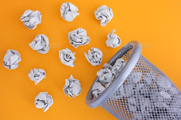Grey crumpled paper balls rolling out of a trash can