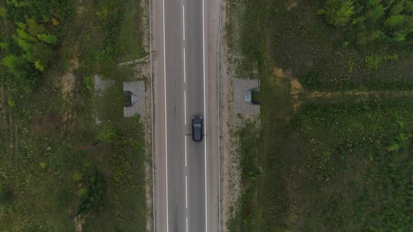 Aerial Following Shot of a Black Sedan Car Driving on an Empty Road Surrounded By a Summer Forest