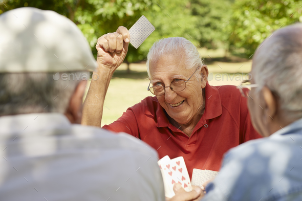Active Seniors Group Of Old Friends Playing Cards At Park