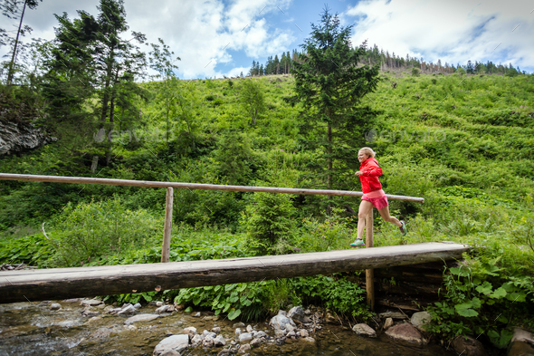 Young woman running on bridge in mountains on summer day