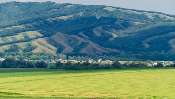 Beautiful Landscape of a Field with Hay Bales Against the Big Hill