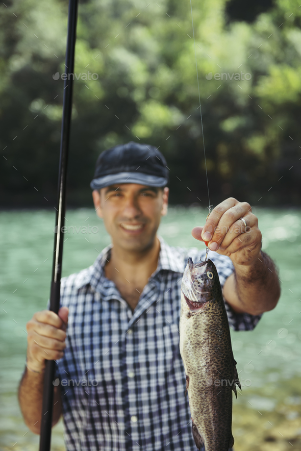 Man Fishing On River And Showing Fish To The Camera Stock Photo by  diego_cervo