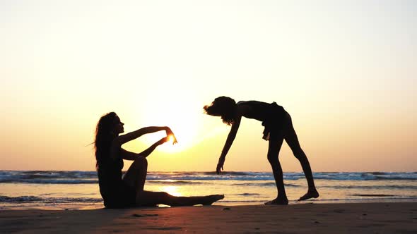 Silhouette of a Woman Trains a Girl to Perform Acrobatic Element on the Beach