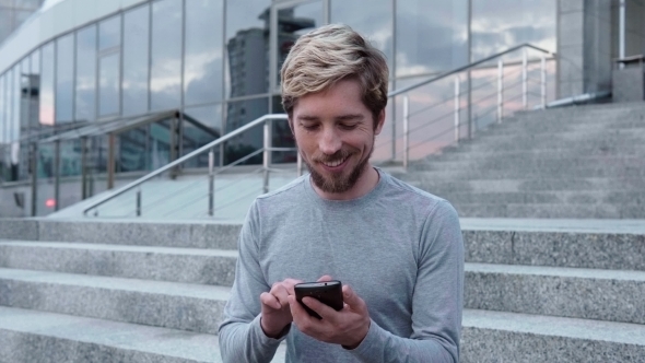 Happy Young Man Hipster Using a Smartphone in City