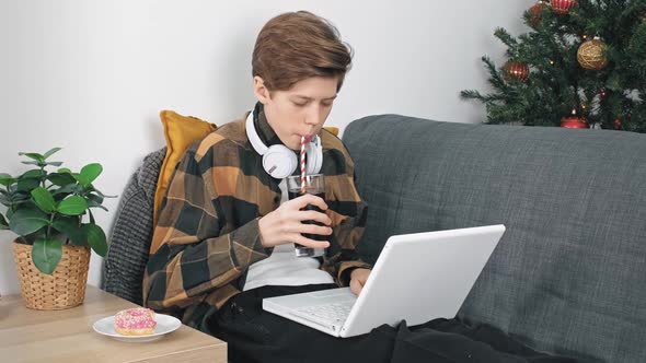 A Teenage Boy with Headphones and a Laptop is Studying Information on the Internet Sitting at Home