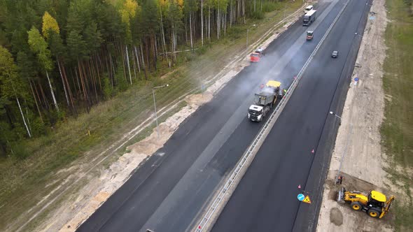 Workers in overalls are laying a new smooth road surface using heavy equipment alt