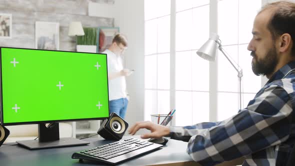 Person Working on PC Display with Green Screen in Cozy Bright Living Room alt