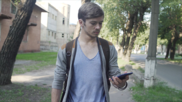 Tired and Stressed Man Walking Down the Street and Chatting with Smartphone