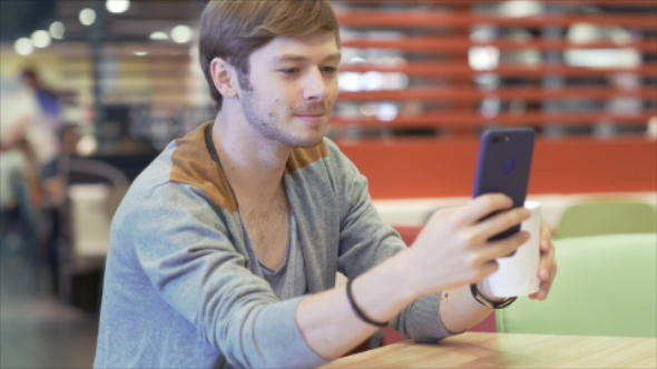 Man with Smartphone drinking Coffee in Fast Food restaurant and gets Stressed while Chatting