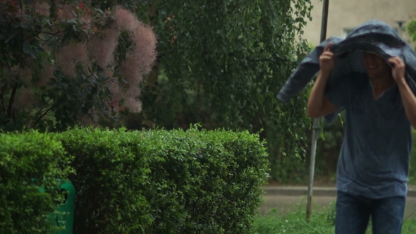 Handsome Man Is Running Across the Street and Hiding From the Rain Under His Jacket