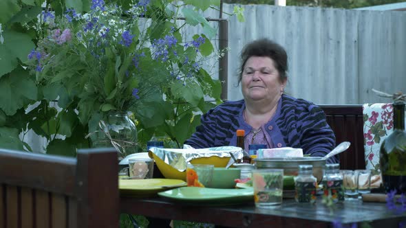 Elderly mature woman sits at dining table in courtyard. Family time at picnic. alt