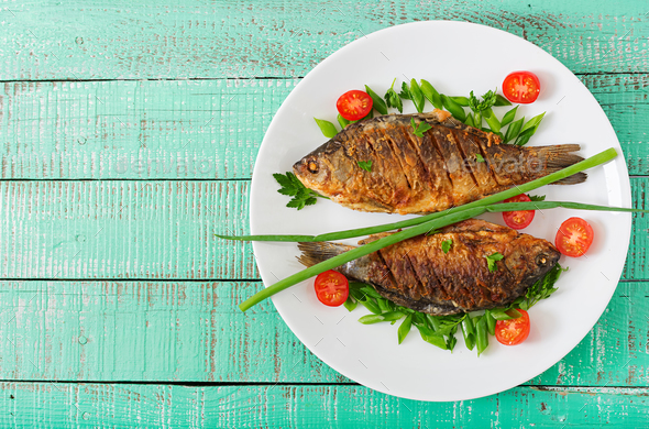 Fried fish carp and fresh vegetable salad on wooden background