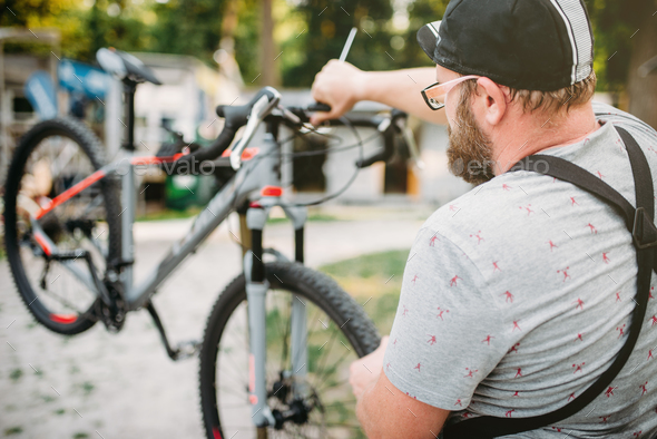 Bicycle mechanic in apron adjusts bike outdoor - Stock Photo - Images