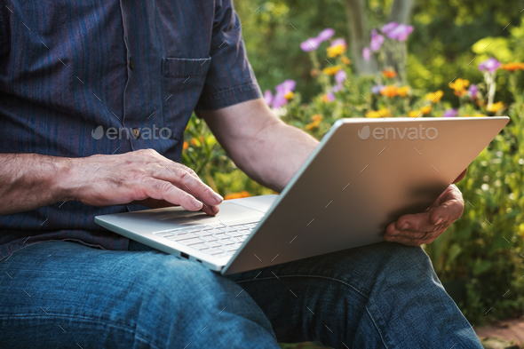 Cropped image of a mature man working on his laptop in garden, old male blogger typing on notebook