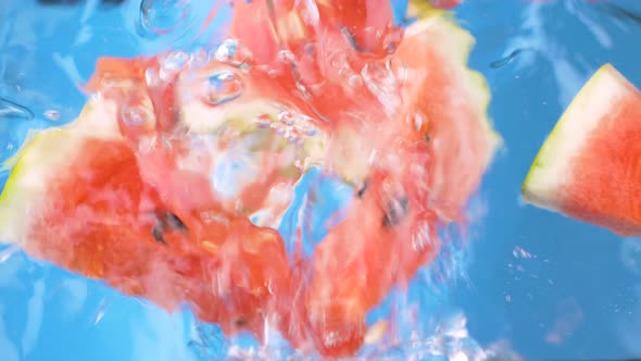 slices of watermelon splashing into the water on blue background alt