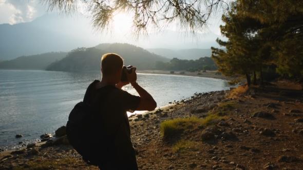 Traveler Photographer Shoots Beautiful Sunset on the Shore of a Mountain Lake alt