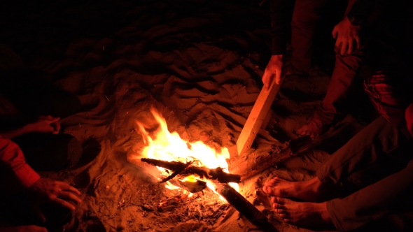 Man Drawing on Sand with a Log Near the Beach Campfire