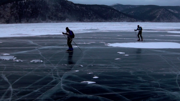 Two Men Are Skating on the Ice of Frozen Lake Baikal During Beautiful Sunset.