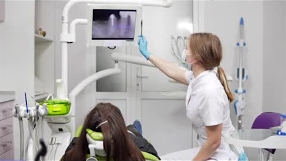 Young Female Dentist Is Showing X-ray Teeth on a Tablet at the Chair. Female Dentist in Mask and Lab alt