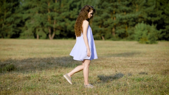 An Adult Girl with Long Curly Hair, Dressed in a Short Sarafan Walks the Field on a Warm Summer Day alt