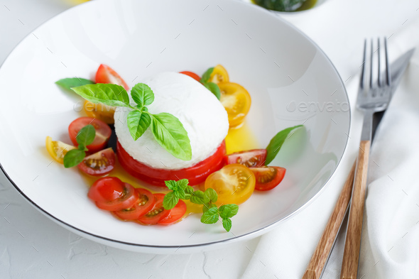 Caprese salad with red and yellow tomatoes, mozarella, basil and olive oil. White background