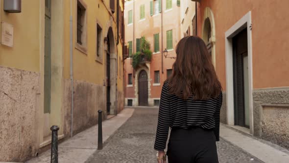 Middle Shot of Back of Brunette Woman Walking on a Narrow European Street