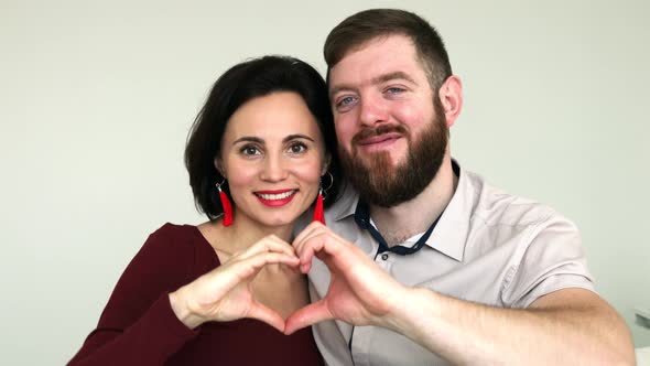 Close up happy lovely couple faces look through joined fingers making heart shape