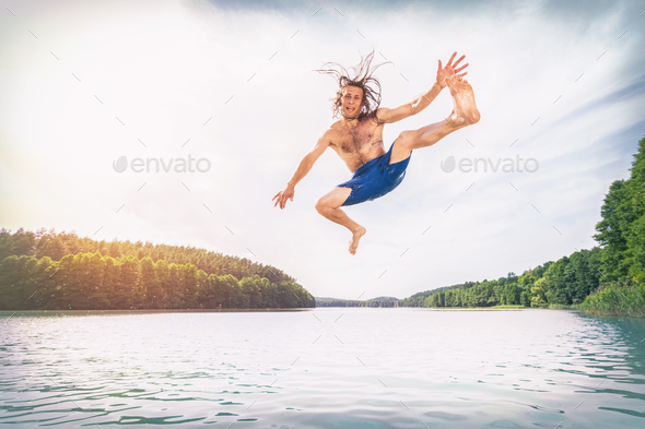 Young fit man making a jump into a lake.