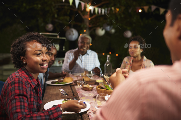Adult black family eat dinner in garden, over shoulder view - Stock Photo - Images