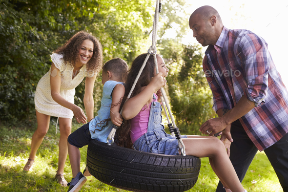 Parents Pushing Children On Tire Swing In Garden Stock Photo By Monkeybusiness