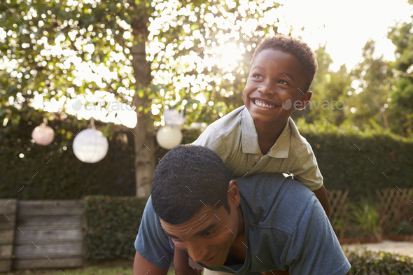 Young black boy playing on his dad’s back in a garden