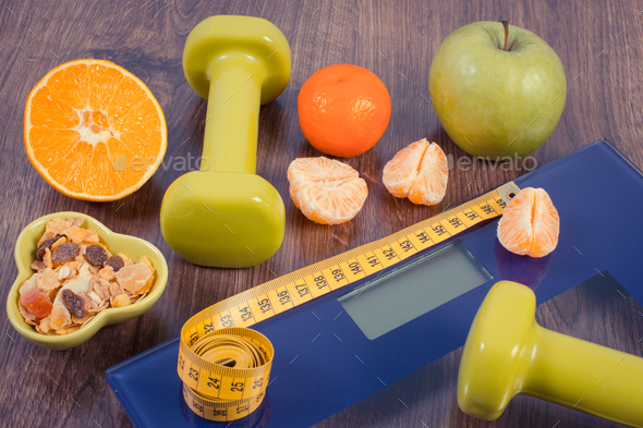 Tape measure on digital scale, dumbbells, fruits and muesli, healthy nutrition and slimming concept