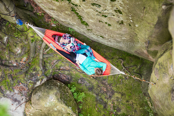 Young women reading books while relaxing in hammock near cliff