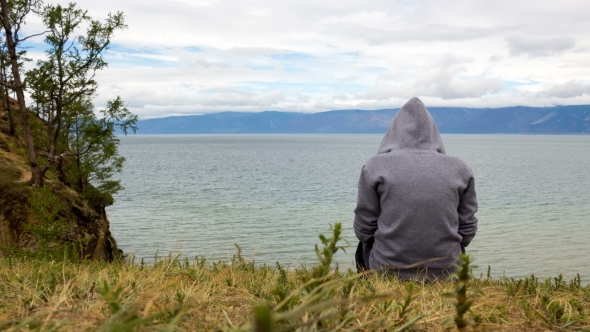 A Man Sits on the Seashore in Cloudy Weather and Contemplates alt