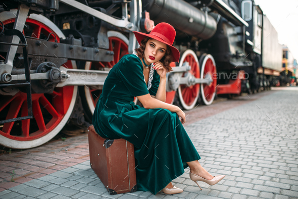 Woman sitting on suitcase against steam train - Stock Photo - Images