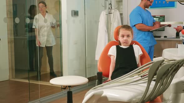 Little Girl Patient Waiting Pediatric Stomatologist Woman Sitting in Dental Chair alt