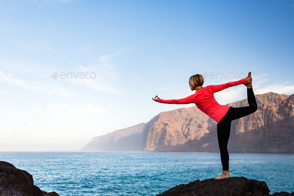 Woman meditating in yoga dancer pose, inspiring landscape