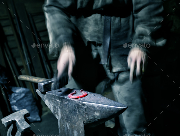 Hands of blacksmith with hammer blowing warmed horseshoe - Stock Photo - Images