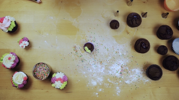 Top View of Chocolate Cupcakes on the Table. Young Woman Decorating Muffins with Colored Cream From alt
