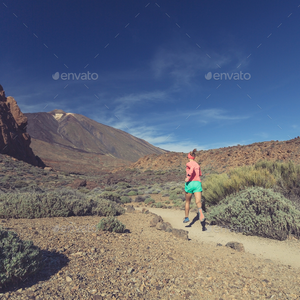 Young woman trail running in mountains on sunny day