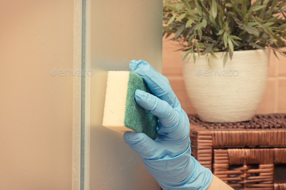 Hand of senior woman using sponge and wiping glass shower door in bathroom, household duties concept