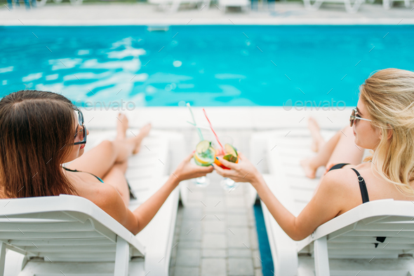 Two sexy girls relax with cocktails on deck chairs - Stock Photo - Images