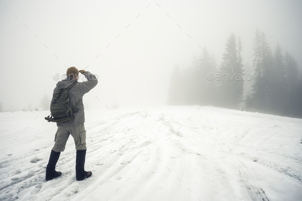 Man with backpack in the winter mountains peers into the foggy d - Stock Photo - Images