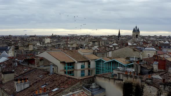 French city of Bordeaux rooftops showing Cailhau City Gate and pigeon flocks flying, Aerial pan righ alt