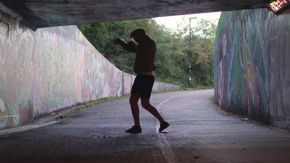 Wide Shot of a Young Athletic Man Boxing in an Underpass, Silhouetted By The Light Behind Him alt
